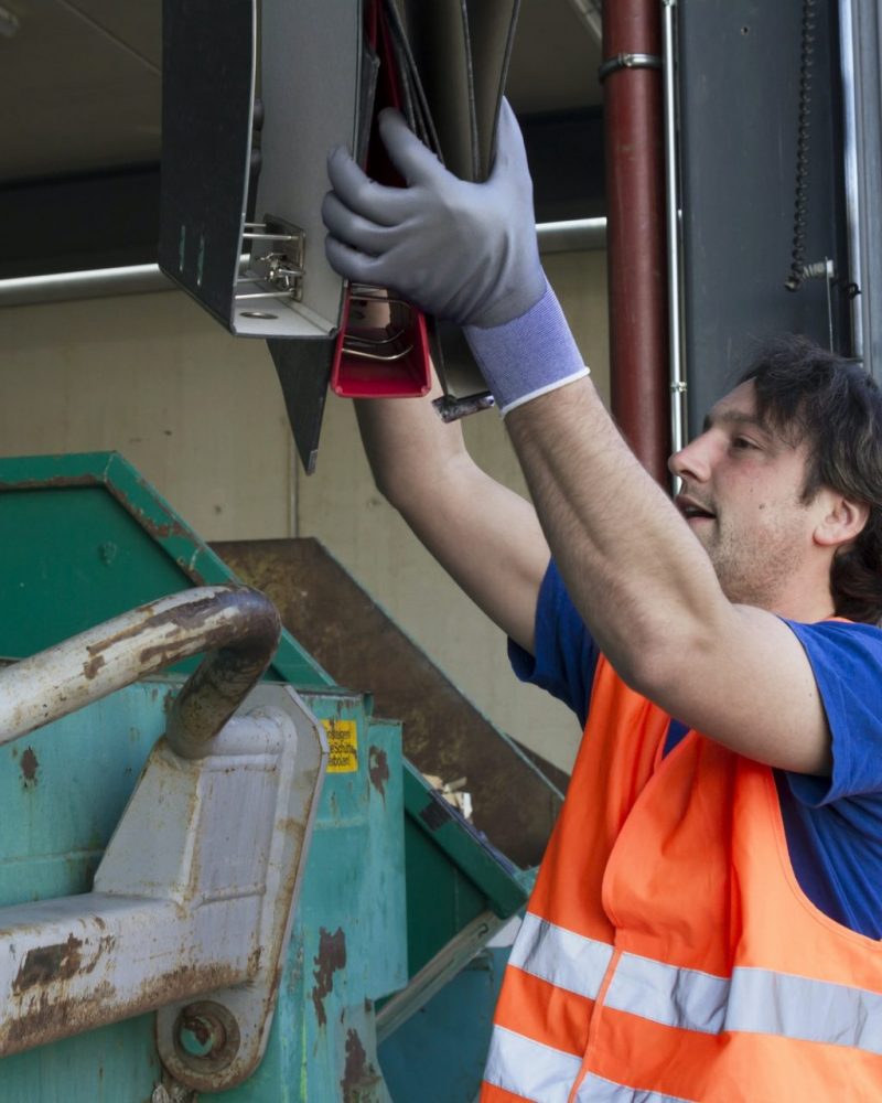 Worker at a waste container throwing away folders